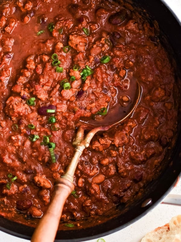 Large pot filled with simmering turkey chili with kidney and pinto beans and garnished with chopped green onions.